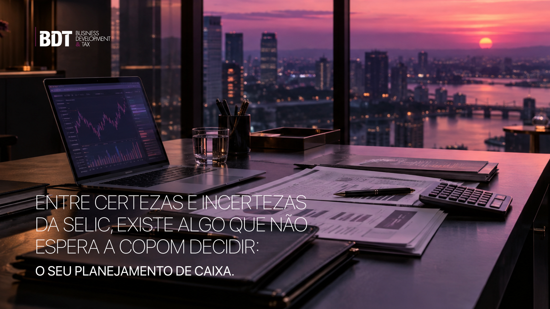 Mesa de trabalho com notebook, gráficos e calculadora diante da cidade ao entardecer: planejamento de caixa diante da Selic